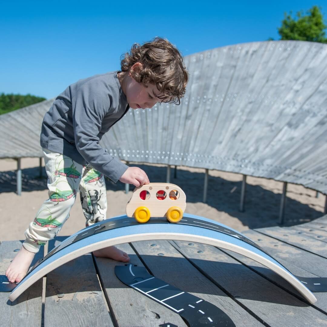 Child using Wobbel Board as bridge and tunnel for wooden vehicle play at Mercurius Australia